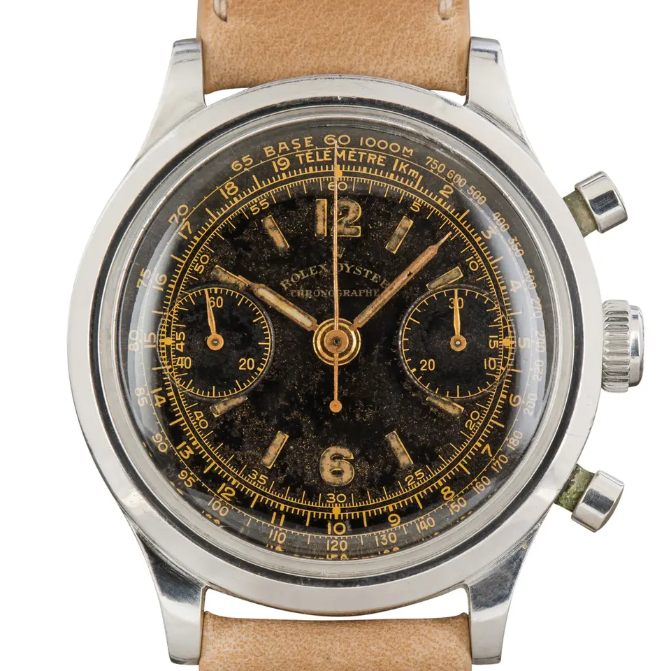 Rolex Chronograph 3525 with a black chronograph dial with gold numerals and tachymeter scale, steel case on a beige leather strap, a pre-owned example, studio close-up of the case