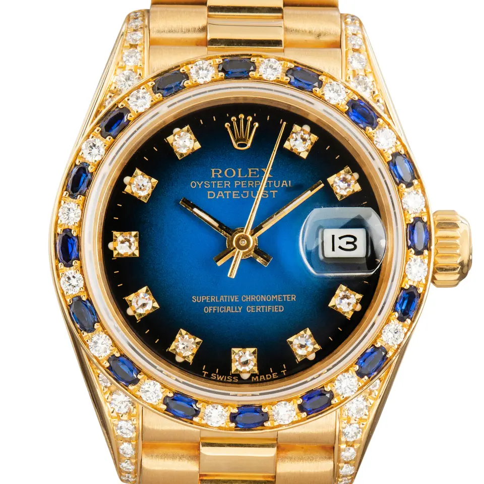 Rolex Lady-Datejust 69238 with a blue vignette dial with diamond hour markers, bezel set with diamonds and sapphires and yellow gold President bracelet, a pre-owned example, studio close-up of the case