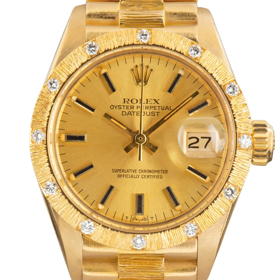 Rolex Lady-Datejust 6927 with a champagne dial with baton markers and a bark-finish yellow gold bezel set with diamonds on a bark-finish yellow gold bracelet, a pre-owned example, studio close-up of the case