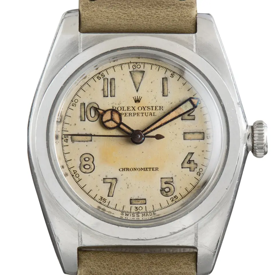 Rolex Oyster Perpetual 2940 with an aged cream Arabic-numeral dial, smooth steel bubbleback case on a leather strap, a pre-owned example, studio close-up of the case