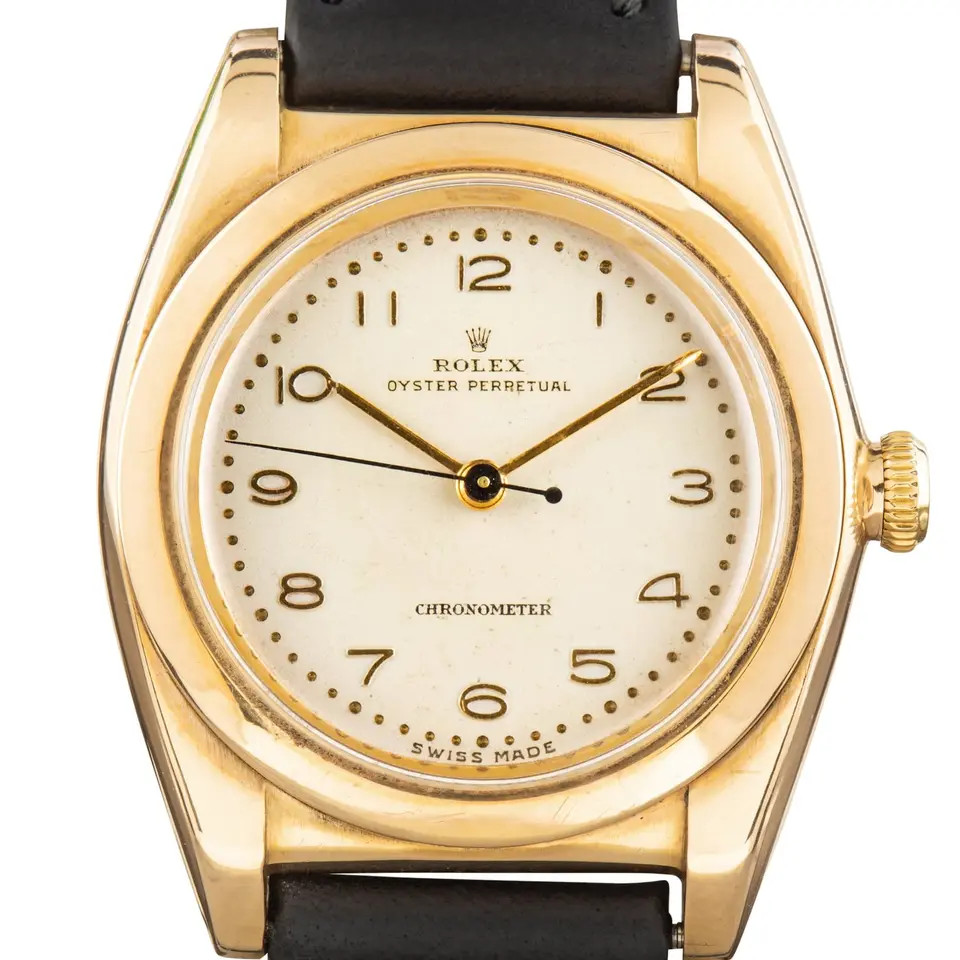 Rolex Oyster Perpetual 3131 with a cream Arabic-numeral dial, smooth gold bubbleback case on a black leather strap, a pre-owned example, studio close-up of the case