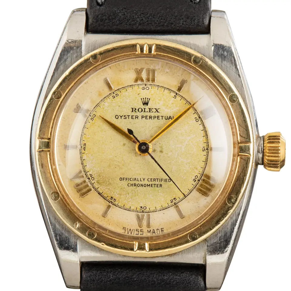 Rolex Oyster Perpetual 32 3372 with an aged cream dial, engine-turned gold bezel and steel and gold bubbleback case on a black leather strap, a pre-owned example, studio close-up of the case