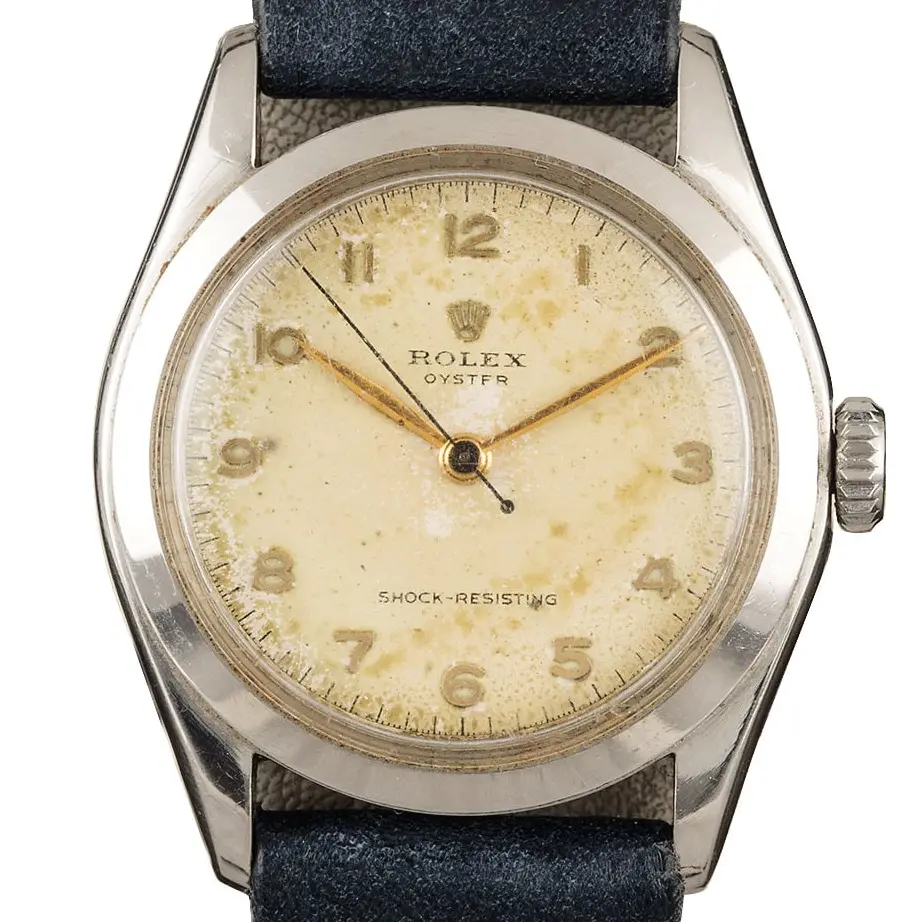 Rolex Oyster Precision 36 6082 with an aged cream Arabic-numeral dial, smooth steel case on a navy leather strap, a pre-owned example, studio close-up of the case